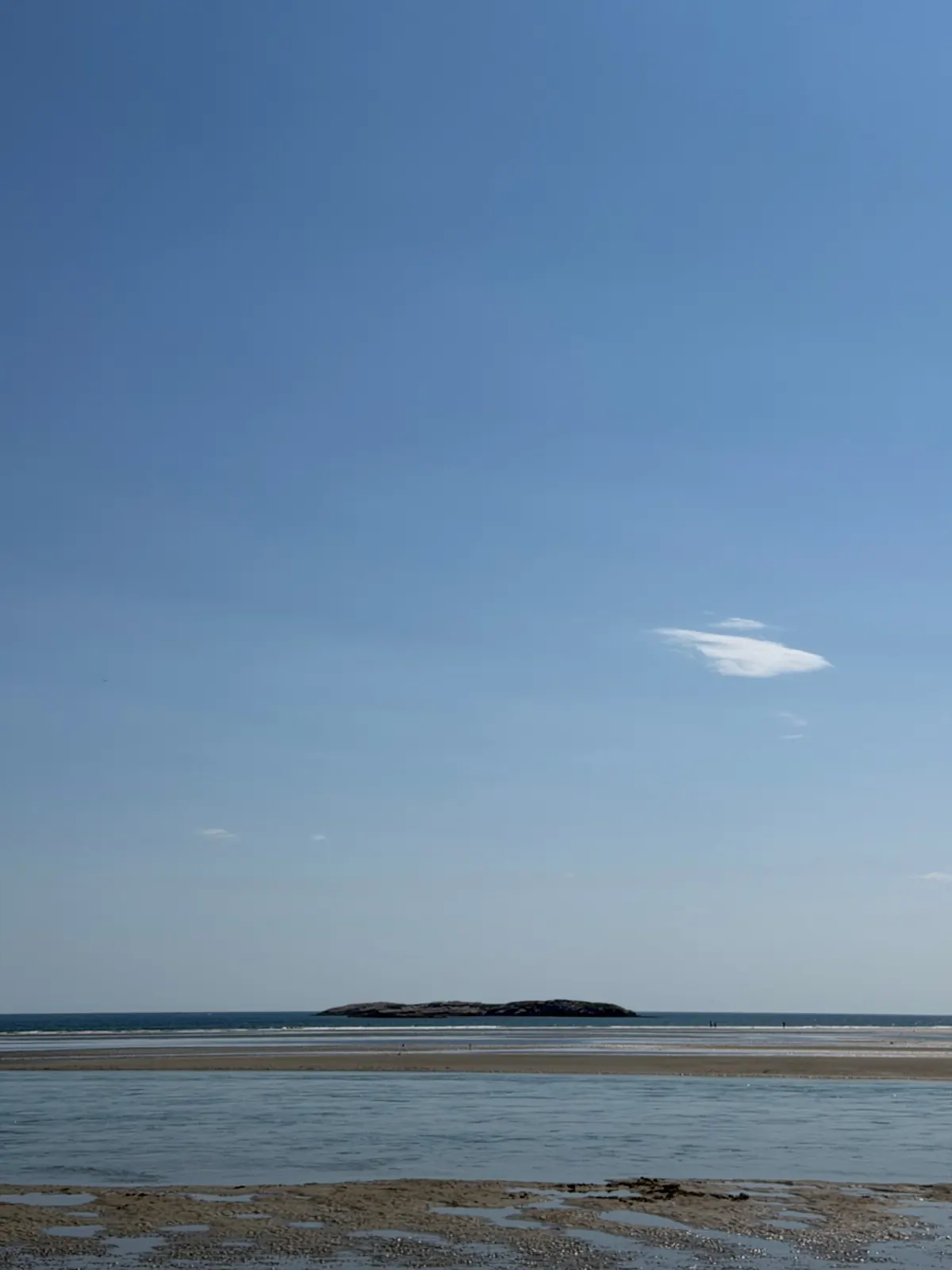 Tidal flats and a low rocky island under a wide blue sky